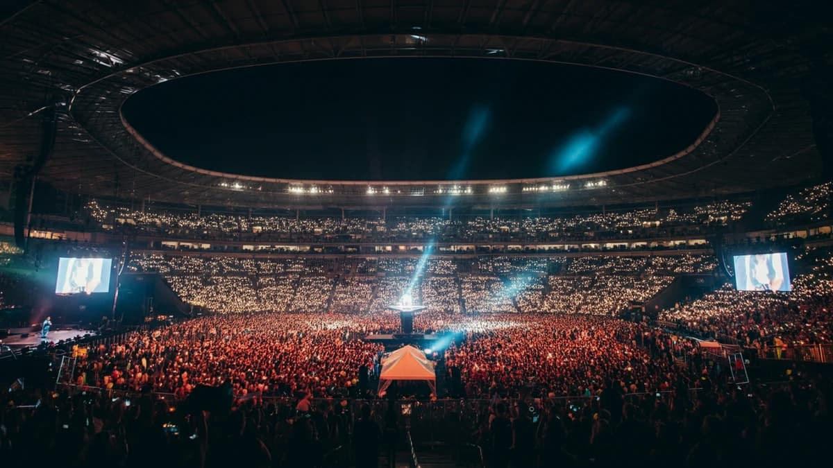 A view from the stage of a massive, sold-out stadium concert at night, with fans holding up glowing phones.